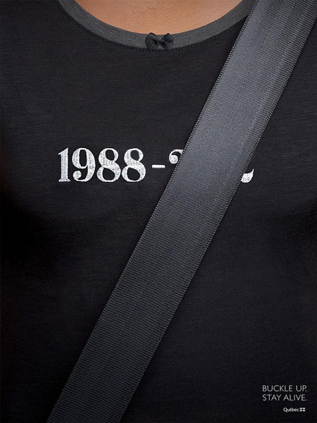 A person wearing a t-shirt that displays a birth year and a death year with the death year covered by a seatbelt to emphasize the message through visuals
